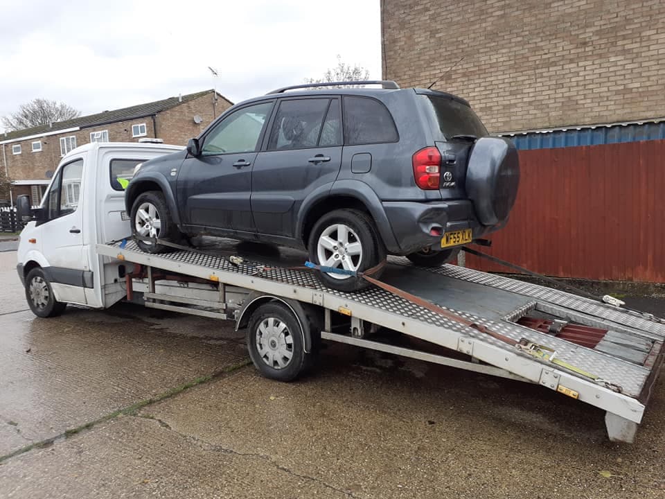 Dark grey SUV secured on the back of a white flatbed transporter