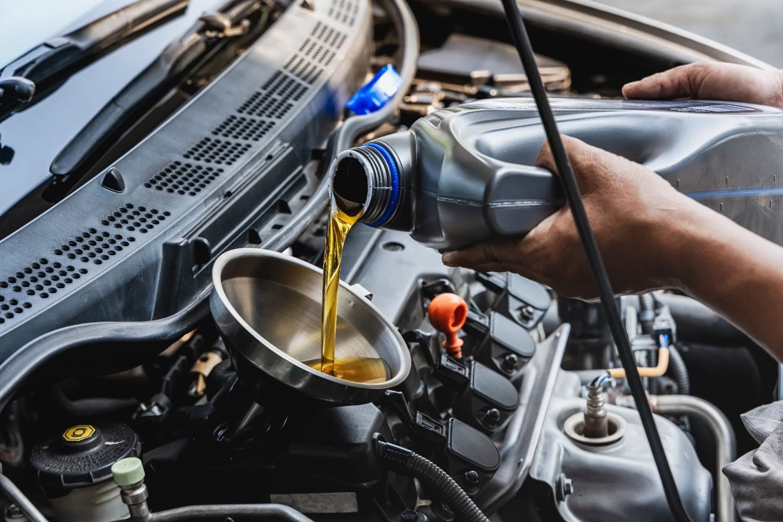 Technician pouring fresh engine oil into a car engine during a service